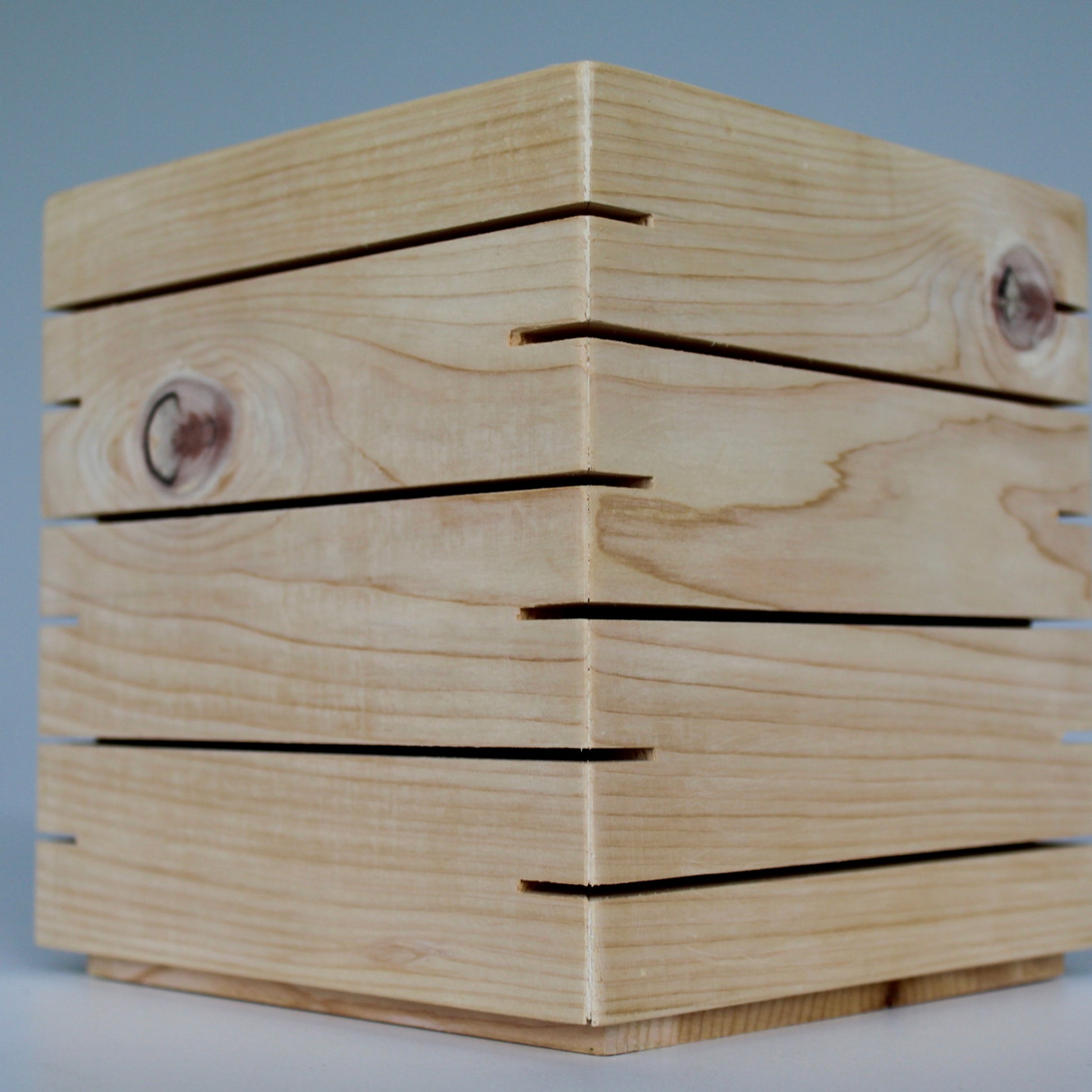 A detailed unlit 3/4 view of 'The Cubenheim' horizontal slit cube light from The Urbanist Series. Handcrafted from premium natural cedar, this shot highlights the raw, intricate beauty of the wood grain and several prominent natural knots. The precisely cut horizontal slits wrap cleanly around the corners of the geometric block, emphasizing the monolithic and architectural quality of the design even when not illuminated. The lamp sits on a clean, neutral surface, showcasing its role as a silent 