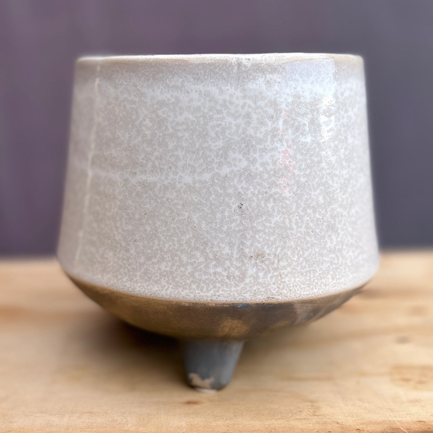 A slightly angled perspective of the empty TV008 Tera-Vessel, highlighting the geometry of its tripod foundation and the textured two-toned speckled glaze. The salvaged ceramic planter sits empty on a wooden surface, serving as a clean architectural shell ready for botanical integration.